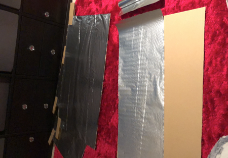 Kitchen foil stuck on a large piece of cardboard box to create a DIY radiator reflector foil to save money on heating costs.