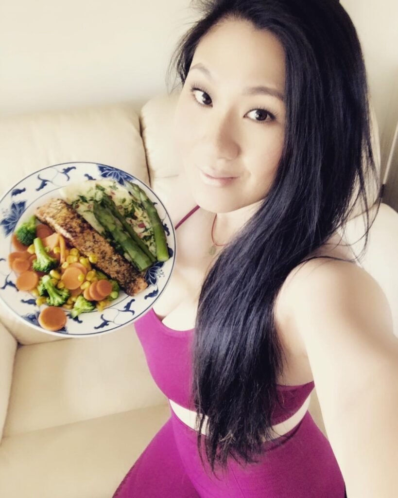 Lei Hang (The Thrifty Island Girl) in red pink seamless Gymshark workout clothing and plate of lunch consisting of salmon filet and vegetables.
