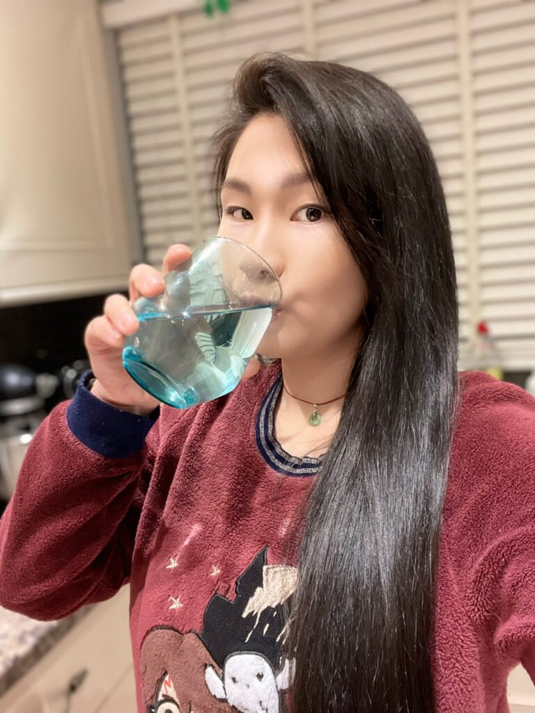 The Thrifty Island Girl Lei Hang drinking Brita filtered water from turquoise tumbler glass in her fleece Harry Potter Pyjamas.