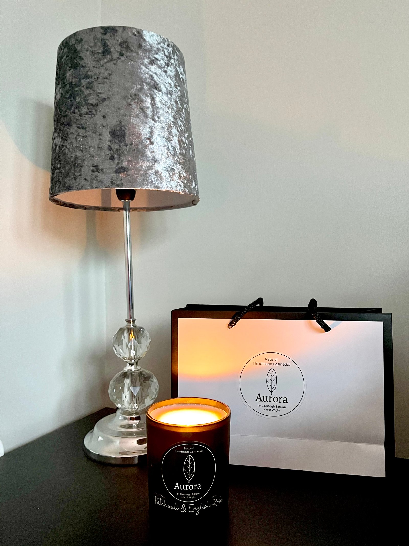 Black aurora cosmetics candle in Lei Hang living room side table with a grey velvet and crystal table lamp and a white aurora paper bag.