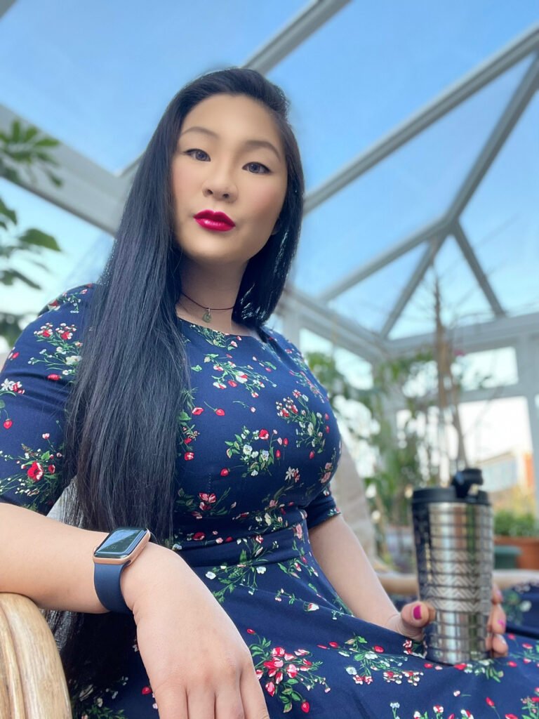 Lei Hang aka the thrifty island girl with long natural straight black hair and red lipstick, wearing a navy blue, floral, tailored dress by the pretty dress company and matching navy blue apple watch series 6, holding the the limited edition nespresso touch mug  with coffee in it. 