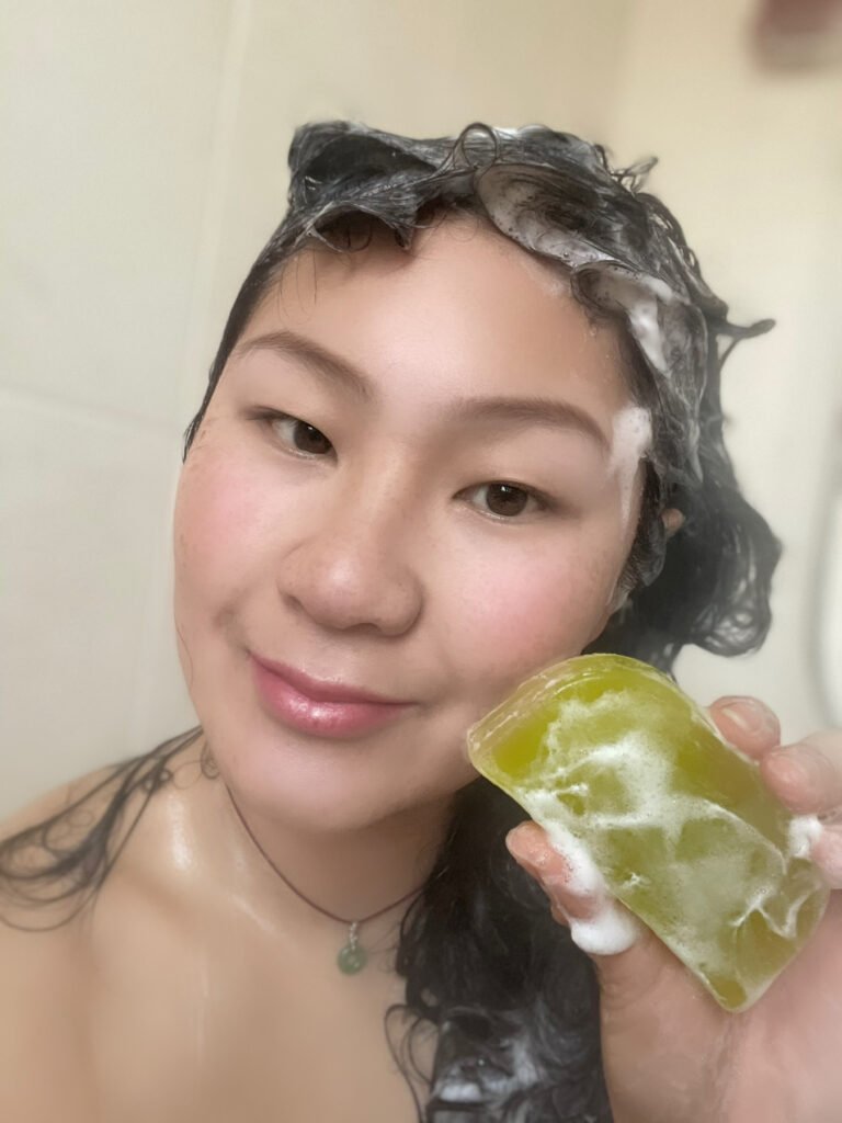 Lei Hang aka The Thrifty Island Girl using a green Aurora solid shampoo bar during her bath.