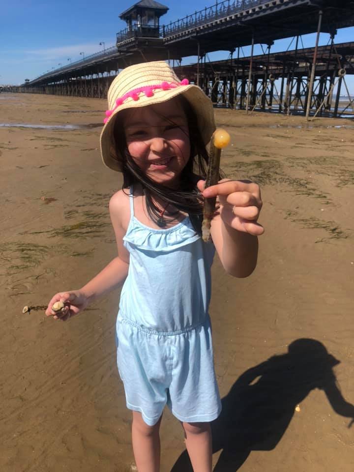 Yasmin wearing a straw hat and light blue playsuit at Ryde beach on the Isle of Wight rock pooling for world oceans day. She found a razor clam.