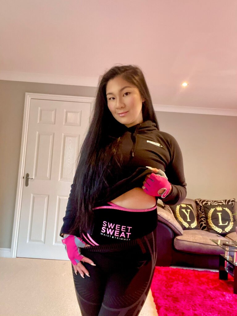 The Thrifty Island Girl Lei Hang wearing a black and pink Sweet Sweat Waist Trimmer by Sports Research to aid weight loss.