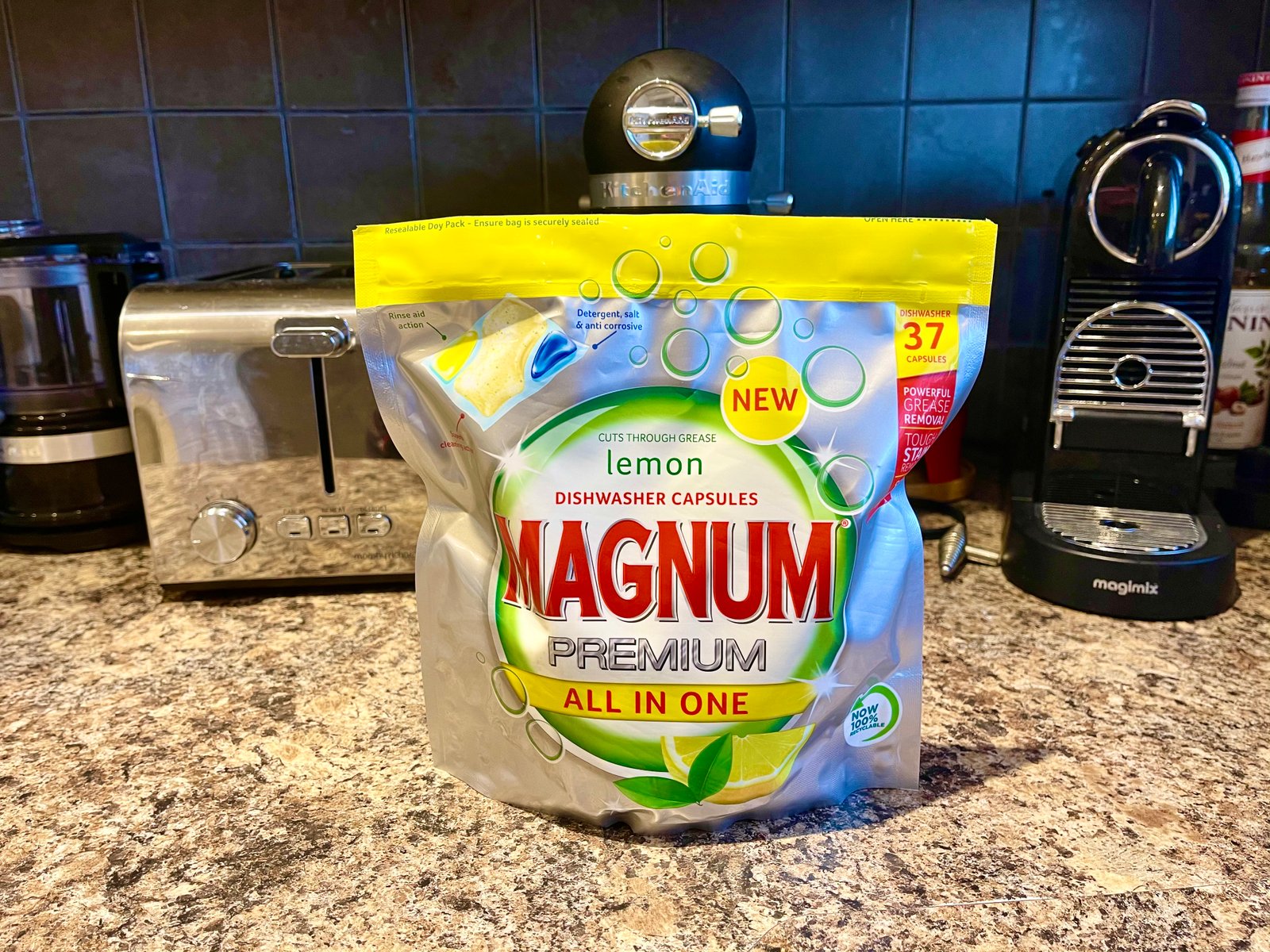 Lei Hang reviews the Aldi Magnum Premium All in One Dishwasher Capsules in lemon scent. Bag of the dishwasher tablets on Lei Hang's kitchen counter with a black and silver nespresso machine and kitchen aid standmixer